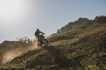 Obraz premium Motocross rider climbing a steep hill in a sunny day