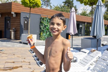 A cheerful young boy enjoying a summer day by the pool, holding an ice cream cone and giving a thumbs up.