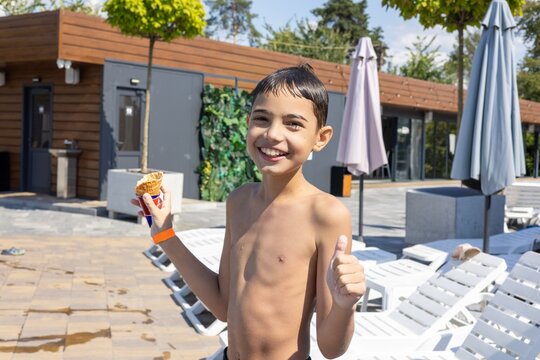 A cheerful young boy enjoying a summer day by the pool, holding an ice cream cone and giving a thumbs up. - Powered by Adobe