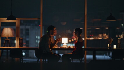 Pair talking night restaurant sitting by panoramic window with city view. 