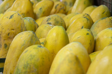 Ripe yellow papayas stacked closely at a local market.