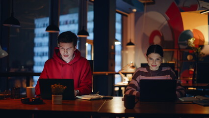 Overtime workers looking laptops in coworking space closeup. Two colleagues late