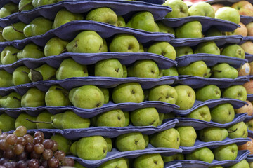 Fresh green pears neatly stacked in purple trays at a market stall.