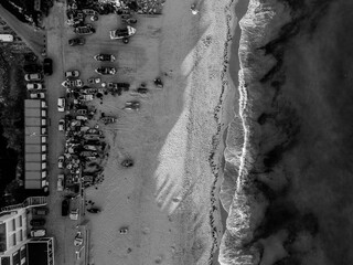Black and white aerial of fishing boats, cars, and waves on sandy beach in Burgau, Algarve, Portugal