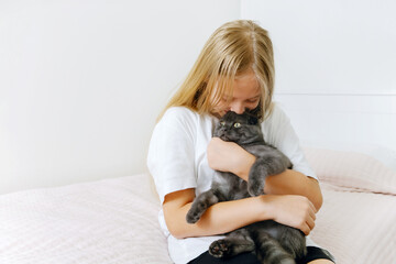 Girl in a light room holding and hugging a gray cat © YouAreMagic Space
