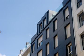 Modern building facade with dark grey tiles and white roller shutters reaching for the sky