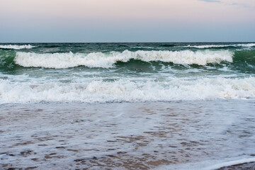Strong ocean waves breaking on sandy beach at sunset