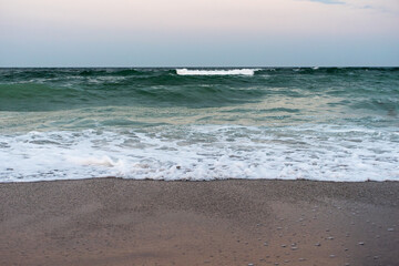 Ocean waves rolling onto sandy beach with foam at sunset