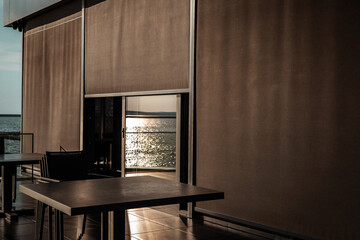 A modern restaurant patio offers a serene dining experience with a sea view. An elegant outdoor dining area with a view of the ocean, featuring tables and chairs and glass railings. A holiday resort.