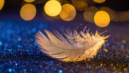 Delicate golden feather rests on sparkling blue glitter with soft bokeh lights