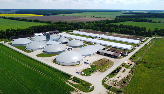 Aerial view of large farm with multiple round and rectangular buildings, surrounded by green fields and farmland, partly cloudy sky, showcasing agricultural infrastructure and rural landscape
