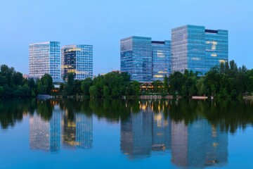 Obraz premium Modern Corporate Office Buildings with Glass Facades Reflecting in Water at Twilight