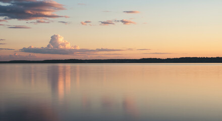 Fototapeta premium A still lake perfectly mirrors the soft, pastel hues of a sunset sky, with a serene horizon line of distant trees, creating a moment of quiet harmony.