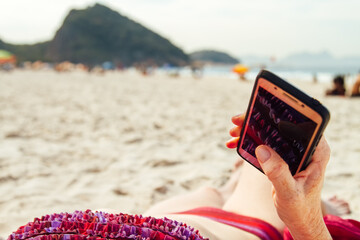 Woman's hand holds a smartphone while sunbathing on a beach in Rio de Janeiro (Brazil)