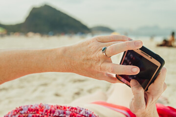 Woman's hand holds a smartphone while sunbathing on a beach in Rio de Janeiro (Brazil)