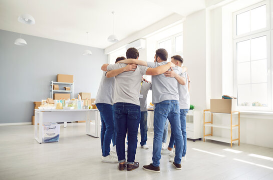 Team of young volunteers standing in circle and hugging. Diverse group standing together, supporting each other, working in humanitarian center. Teamwork, unity, social help, volunteering concept.