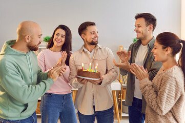 Group of friends celebrates a man birthday at home, surprising him with a cake adorned with candles. The joyous event marks a special anniversary, creating happy memories among friends.