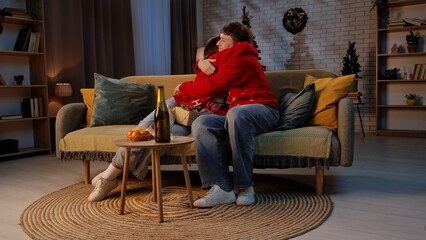 Obraz premium Couple of man and woman celebrating new years eve at cozy home, resting on the sofa together, drinking champagne and hugging.