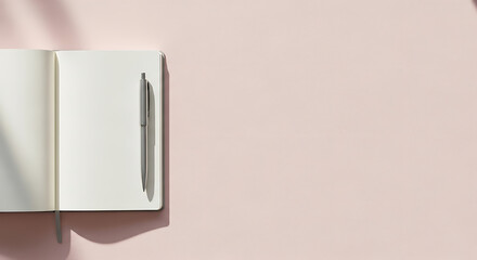 An open notebook with blank pages and a pen lies on a pastel pink background with soft shadows.