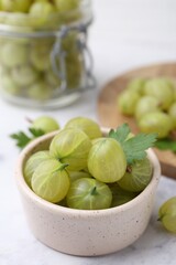 Fresh green gooseberries in bowl on white table, closeup