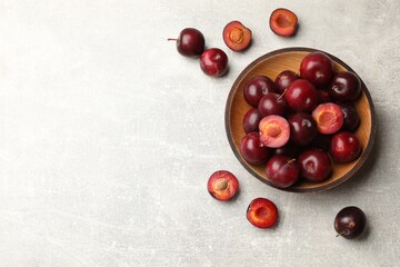 Ripe cherry plums and bowl on grey textured table, flat lay. Space for text
