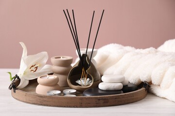 Composition with incense sticks, burning candles and spa stones on white wooden table against pink background, closeup