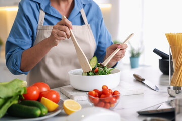 Senior woman cooking salad at white marble table in kitchen, closeup