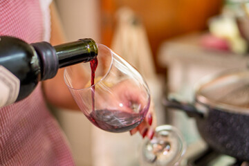 Woman pouring red wine into glass for lunch in kitchen