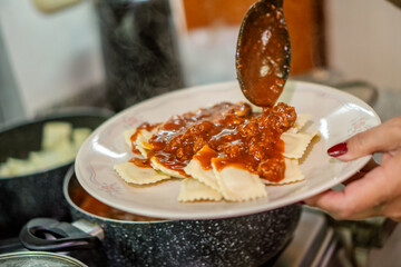 Chef pouring red meat sauce on ravioli for lunch preparation