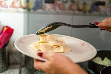 Chef serving ravioli with meat sauce on plate