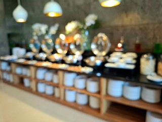 A blurry, out-of-focus photo of a buffet table in a hotel restaurant, showing bowls, plates, coffee, desserts, breakfast items, and beverages. As a background photo, the viewpoint is at eye level.