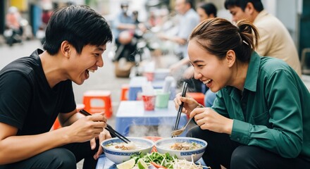 A happy young Asian couple laughing and enjoying a meal of hot steaming noodle soup at an outdoor street food stall.