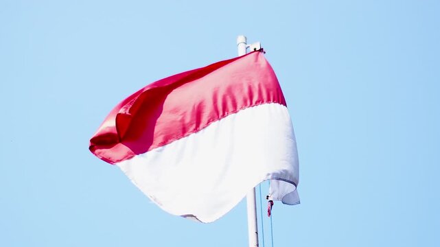 A cinematic video of the Indonesian national flag, red and white, waving gracefully in the wind. Set against a bright blue sky, this footage symbolizes patriotism, freedom, and unity of Indonesia