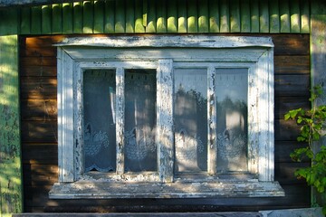 A wooden house in Russia in the summer, lace curtains on the window, the paint peeled off, sun glare on the glass. Comfort, home, village life. Peaceful life