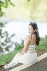 Naklejka premium Woman in a long light dress is resting by the lake enjoying the view.