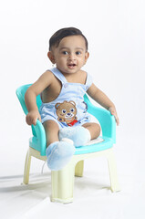 Baby boy sitting in small green chair indoor.