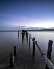 Serene twilight view of a decaying wooden pier extending into calm water under a twilight sky