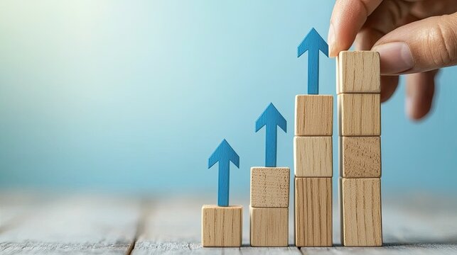 A hand placing wooden blocks with upward arrows on a wooden surface against a blue background. - Powered by Adobe
