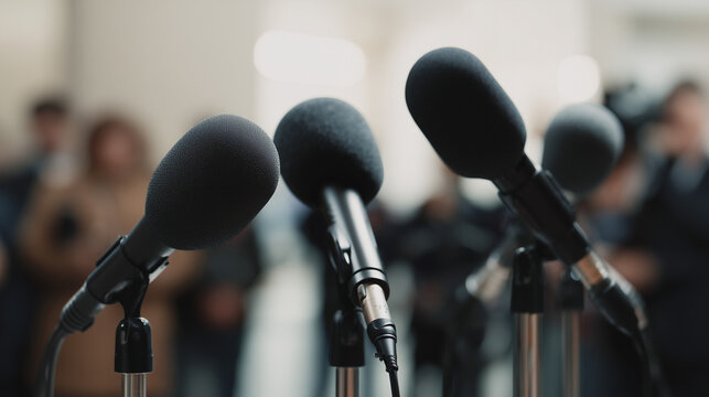 Close-Up Professional Microphones – Black Foam Windscreens on Stands with Blurred Audience Press Conference Scene