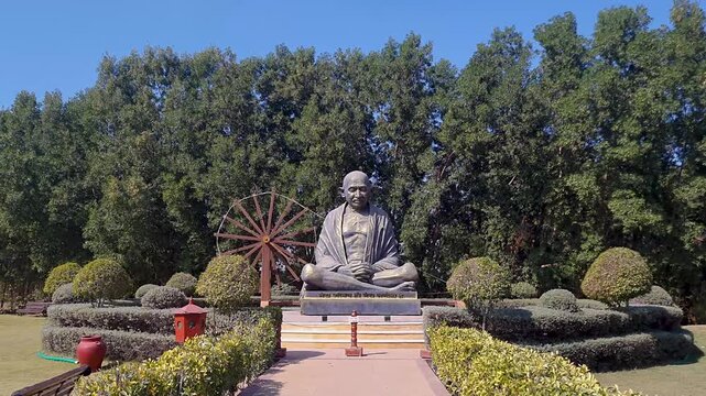 isolated stone statue of Mahatma Gandhi with traditional spinning wheel at day