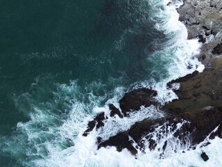 Aerial view of ocean waves crashing on rocky coastline, seascape with cliff, surf, splash, foam, beach rocks, wild sea, scenic landscape, nature background, drone photography