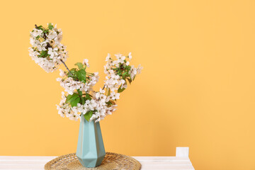 Vase with blossoming branches on shelf near orange wall in room