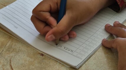 A female student's hand is writing a story in a notebook in classroom.