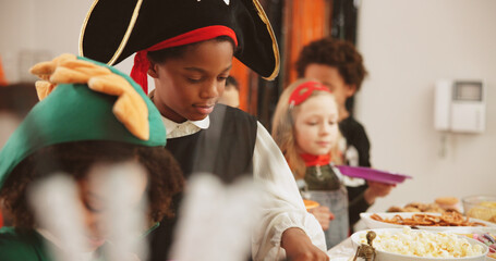 Halloween party, food and kids with boy, celebration and hungry with tradition. Friends, home and children with snack, costume and sweets with treat, happiness and fantasy with fun, candy and popcorn