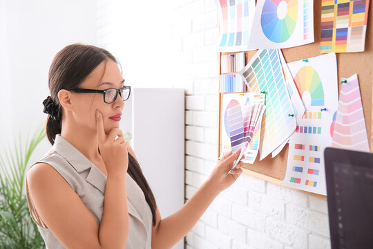 Thoughtful Asian graphic designer with color palettes in office
