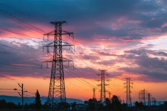 Power lines stretch across a colorful sunset sky with hues of orange pink and gray clouds - Powered by Adobe