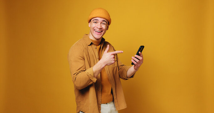 Pointing, phone and portrait of man in studio for online notification, website and communication. Mockup, space and person with gesture, shocked and happy on smartphone for social media, post or news