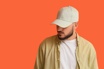 Handsome young man in stylish cap on orange background