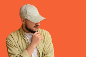 Handsome young man in stylish cap on orange background