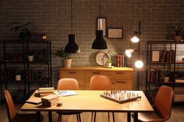 Interior of dark room with bookshelves, table and glowing lamps at night